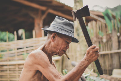 Shirtless man smoking bidi while holding hammer outdoors