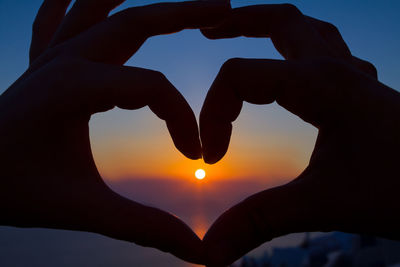 Silhouette hand holding heart shape against sky during sunset