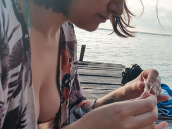 Midsection of woman holding marijuana sitting on pier against sea