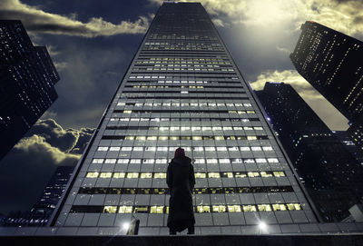 Low angle view of woman looking at modern building against sky in city