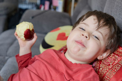 Expressive young boy eating an apple and lounging on the couch at home