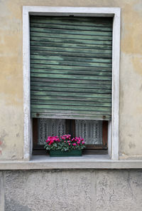 Rectangular window with broken blind of an old house with a balcony embellished