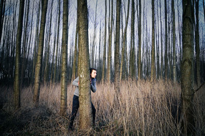 Young man behind tree in forest