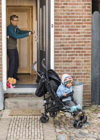 Man with granddaughter sitting in baby stroller outside house