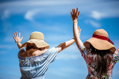 Rear view of women with arms raised standing against sky