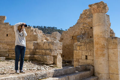 Full length of woman photographing while standing in old ruins