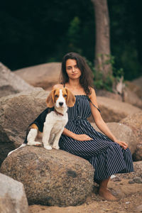 Portrait of young woman with dog sitting on rock