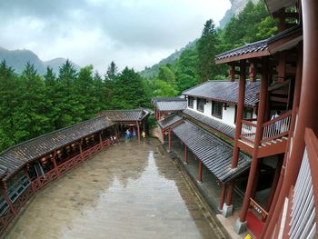 Footbridge amidst trees and buildings against sky