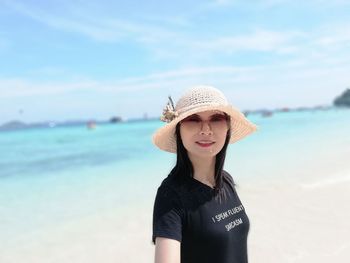 Portrait of beautiful young woman standing at beach against sky