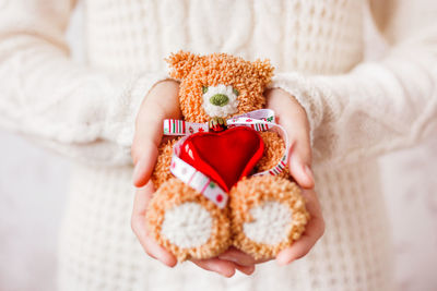 Woman holds hand made crocheted toy bear with christmas ribbon and red heart. present for kid.