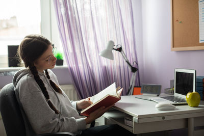 A teenager reads her school reading in her room at home.