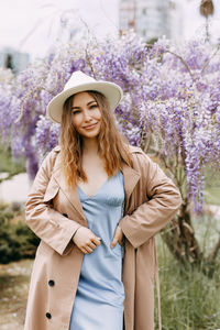 Gentle girl in a dress and a fashionable hat is walking enjoying the smell of flowers in the park