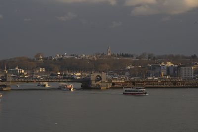 Boats in river by cityscape against sky