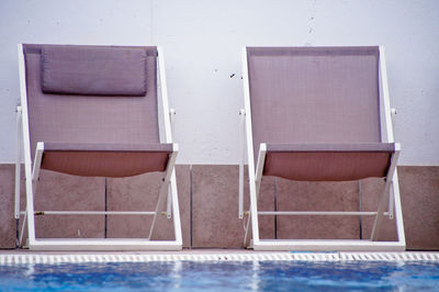 Empty chairs in swimming pool against building