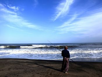 Person standing on beach with fishing pole