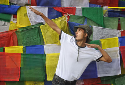 A indian young guy making dab gesture, posing against tibetan buddhist prayer flags with copy space 