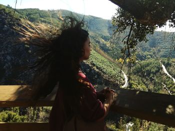 Side view of young woman standing by tree against sky