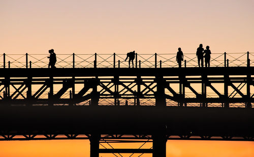 Silhouette of people on bridge against sunset