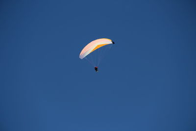 Low angle view of paragliding against clear blue sky