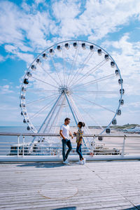 People with ferris wheel against sky