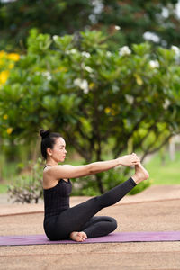 Young woman sitting on plant against trees