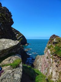 Rock formations by sea against clear blue sky
