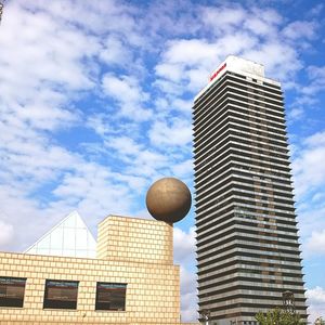 Low angle view of modern buildings against cloudy sky