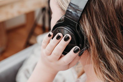 Caucasian teenager girl with black headphones enjoying music at home. unrecognizable person