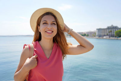 Portrait of smiling young woman standing against sea