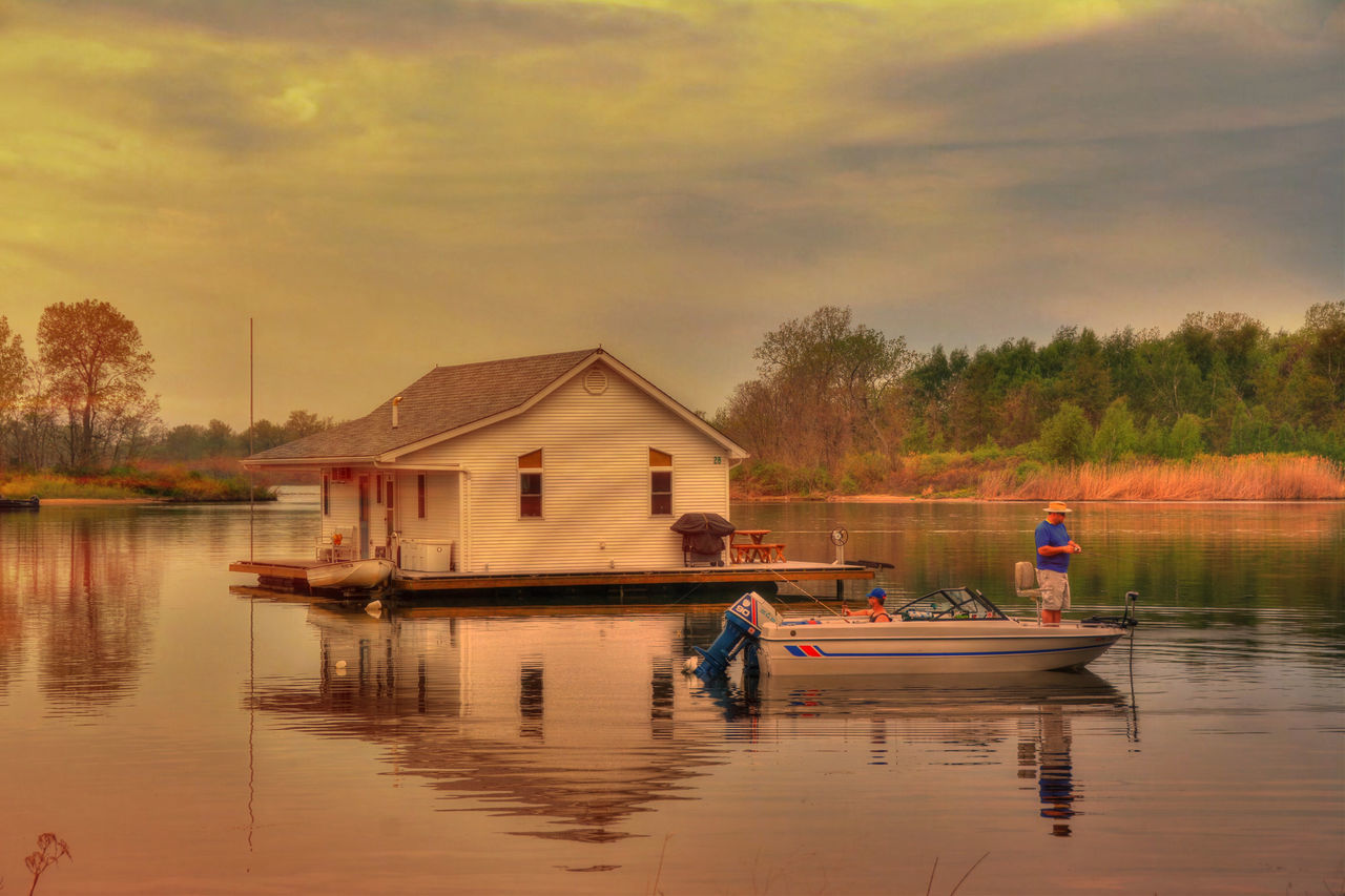 water, lake, lifestyles, men, leisure activity, tree, sky, built structure, building exterior, reflection, architecture, waterfront, person, rear view, river, nautical vessel, sitting