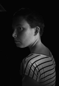 Side view of thoughtful woman standing against black background