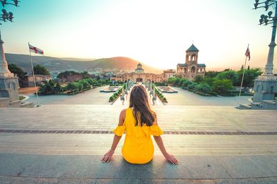 Rear view of woman sitting against buildings in city