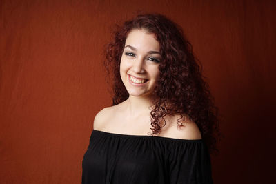 Portrait of smiling young woman against brown background