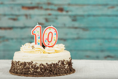 Number 10 candle on birthday cake over table against wall