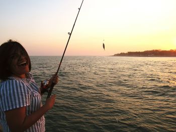 Woman fishing at sea during sunset