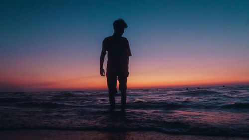 Silhouette man standing on beach against sky during sunset