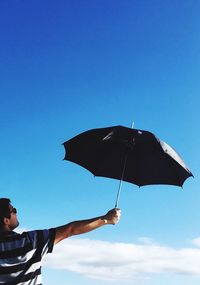 Side view of mature man wearing sunglasses holding umbrella against blue sky