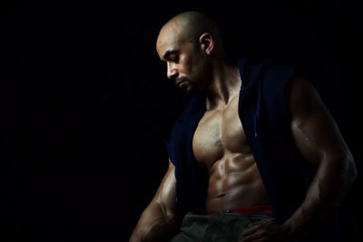 Muscular man sitting against black background