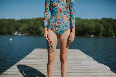 Midsection of woman standing on pier over lake against sky