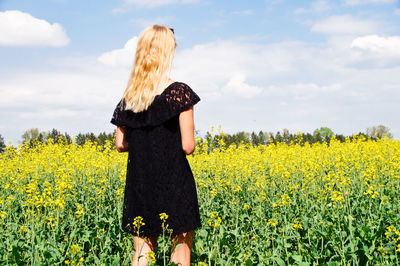 Rear view of young woman standing on oilseed rape field