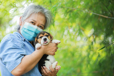 Senior woman wearing mask holding puppies standing outdoors