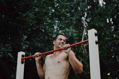 Happy shirtless man doing chin-ups at outdoor