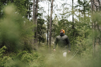 Mature man looking up while exploring amidst trees in forest