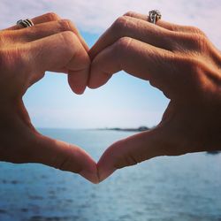 Cropped image of hand holding heart shape against sea