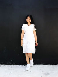 Portrait of a smiling young woman standing against white wall