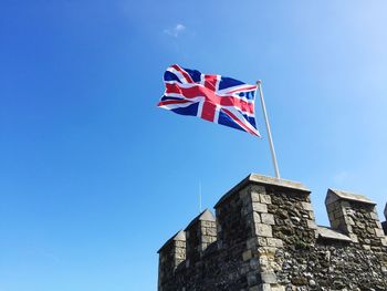 Low angle view of union jack flag flying in the wind on top of a castle against clear blue sky