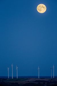 Windmills on field against full moon in clear blue sky at dusk