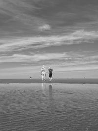 Rear view of man and woman standing at beach against sky