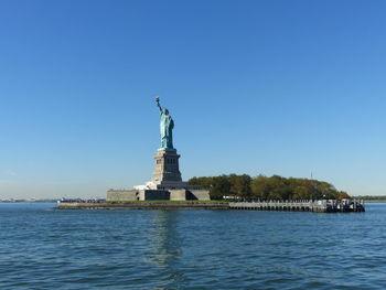 Statue of liberty by hudson river against blue sky