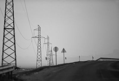 Electricity pylon by road against clear sky